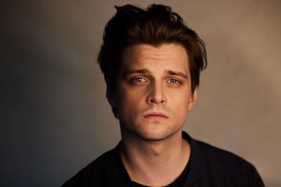 Portrait von Julian Koechlin. Er ist mittig abgebildet und blickt nachdenklich in die Kamera, Schlagschatten im Gesicht. 