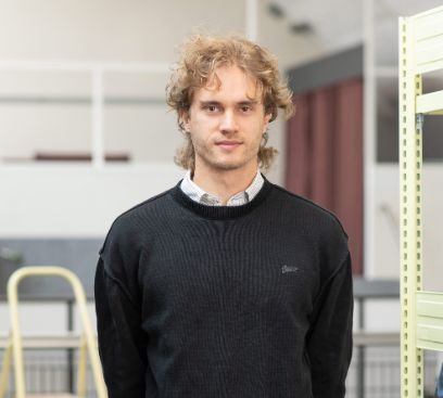 Der junge Mann in dunklem Pullover blickt freundlich in die Kamera. Er hat dunkelblondes, leicht krauses Haar.