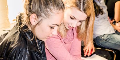 Zwei junge Frauen schauen nach unten und besprechen etwas.