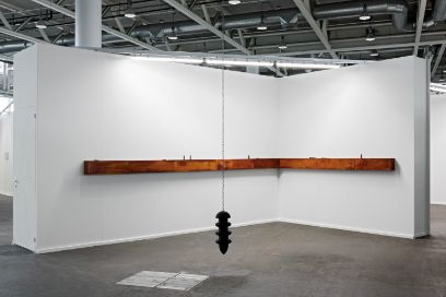 An der weissen Wand, die den Ausstellungsraum der Künstlerin darstellt, hängt die Holzkonstruktion (eine Art Leiste über Eck). Davor hängt das Pendel. Bild: Bundesamt für Kultur, Swiss Art Awards 2026, Gina Folly