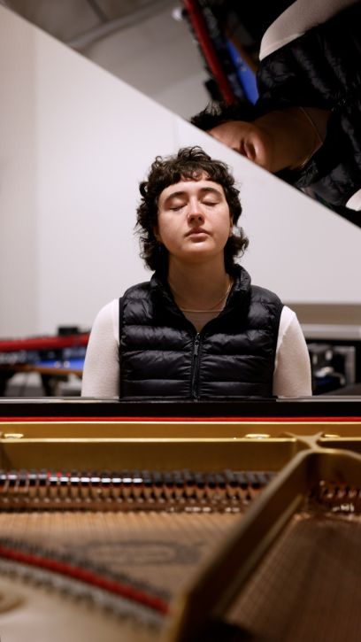 Die dunkelhaarige Frau sitzt am Flügel, der den Deckel geöffnet hat. Ihre Augen sind geschlossen, sie wirkt konzentriert und entspannt zugleich.