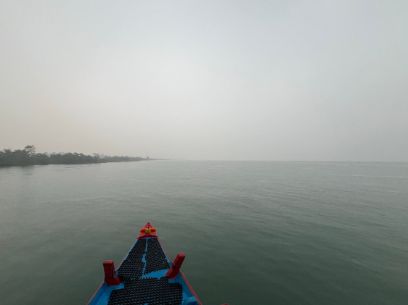 Der Bug eines Bootes auf einer weiten Wasserfläche, links ist das Ufer zu sehen, der Himmel ist verhangen.