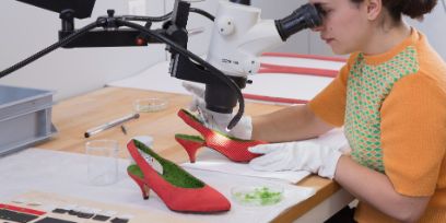 Studentin bei der Arbeit am Mikroskop. Rote Schuhe werden mit grünem, weichem Material ausgekleidet.