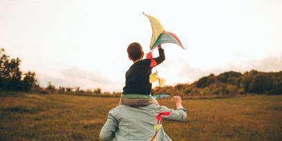 Vater mit Kind auf Schultern beim Drachensteigenlassen