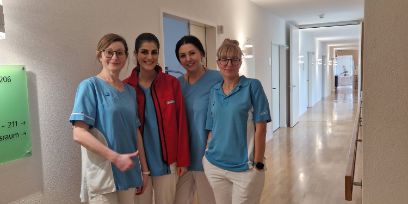 Vier Frauen stehen in einer Pflegeeinrichtung nebeneinander im Flur und lachen in die Kamera