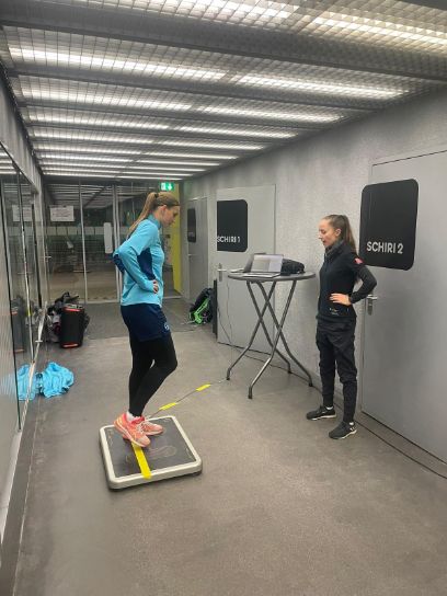 Eine Fussballerin führt einen Sprung-Test aus, während eine andere Frau sie dabei beobachtet.