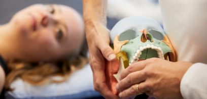 Beispielbild Craniocervicale Dysfunktionen, Studienleiterin zeigt am Schädel physiotherapeutische Behandlung