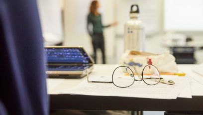 Laptop, Brille, Wasserflasche und Schreibzeug auf einem Pult