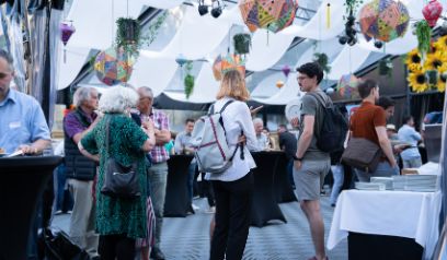 Mehrere Personen an einem Apéro in einem grossen, hellen Raum. Es hat Sonnenblumen und von der Decke hängen farbige Regenschirme und Blumentöpfe als Dekoration.