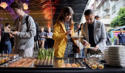 Drei Personen vor einem Tisch mit verschiedenen Apéro-Häppchen. Im Hintergrund sind weitere Personen zu sehen.