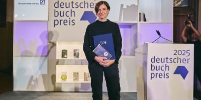 Eine Frau steht auf der Bühne und hält ein Buch in der Hand.