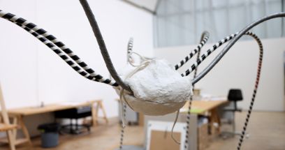 Foto des Kunstwerks «Opi Louise», der Spinne. Der Körper ist weiss (Gips?) und die Beine sind schwarz und schwarz-weiss gestreift. Im Hintergrund sieht man den Raum mit Tischen und Stühlen.