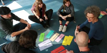 Eine Gruppe von Jugendarbeiterinnen und Jugendarbeiter sitzt in einem Kreis am Boden und diskutiert das Thema Genderreflektierende Jugendarbeit.