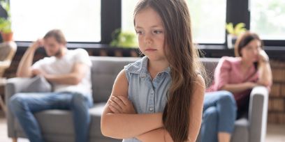 Kind mit verschränkten Armen im Vordergrund, Eltern hinten auf einem Sofa sitzend