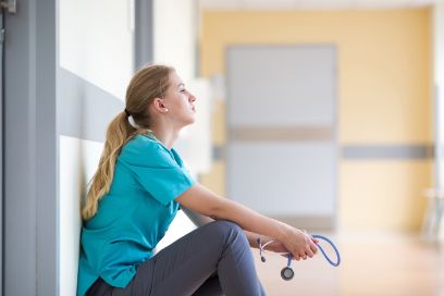 Eine Pflegefachfrau sitzt müde im Gang eines Spitals.