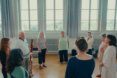 Eine Gruppe aus älteren und jüngeren Menschen steht im Kreis und musiziert und singt gemeinsam.