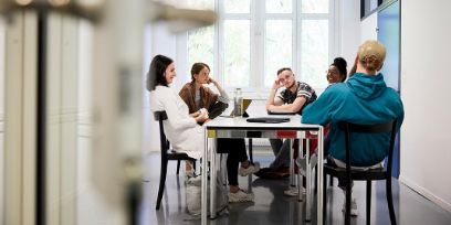Fünf Personen sitzen in ein Gespräch vertieft an einem Tisch.