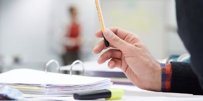 Eine Hand hält einen Stift. Sichtbar ist auch ein Ordner.
