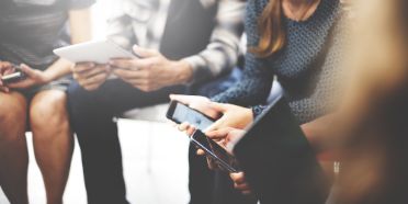 Vier Menschen sitzen beieinander und arbeiten an ihren Smartphones bzw. Tablets miteinander.